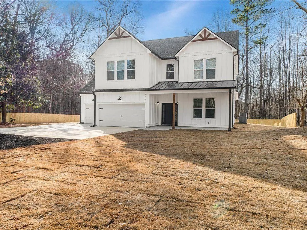 A completed two-story modern farmhouse built by HOC Build: white board-and-batten siding, dark standing-seam porch roof, timber gable brackets and black-framed windows, on a wooded lot.