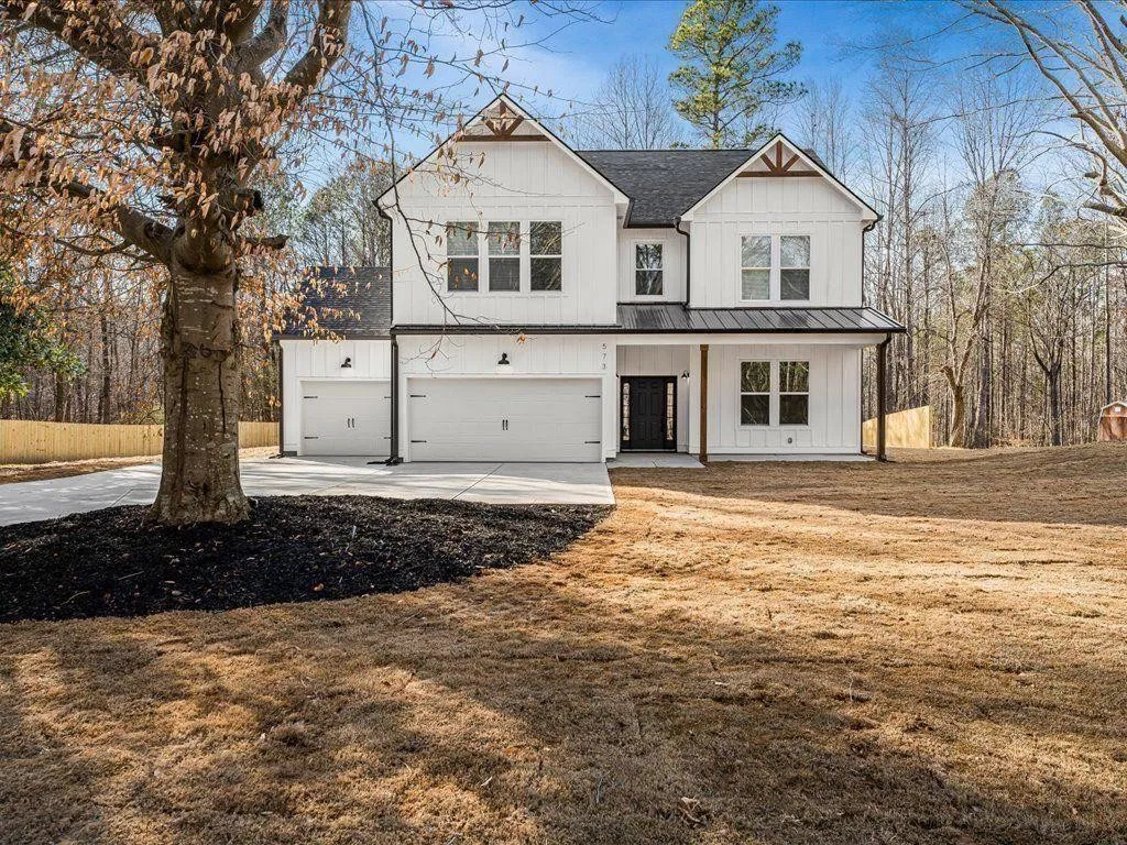 Front elevation of a completed HOC Build home: board-and-batten siding, covered porch with timber posts, three garage bays.